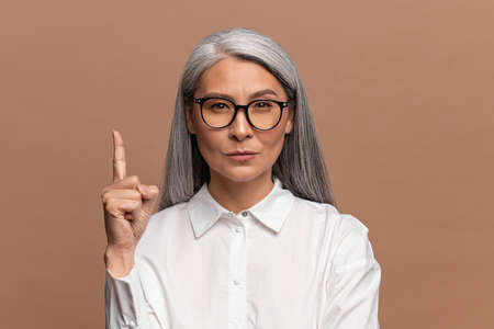 Eureka. Portrait of inspired asian mature woman with long grey hair pointing finger up with genius...
