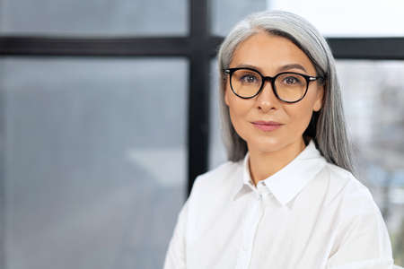 Portrait view of confident and smiling old senior business woman wearing glasses looking at the...