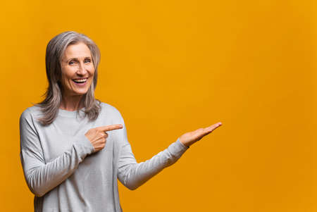 Wow look, advertise here. Portrait of amazed cute woman pointing to empty place on background, surprised lady showing copy space for promotional ad. Indoor studio shotの写真素材