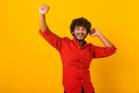 Excited positive bearded hispanic man in stylish clothes dancing, raising hands up and having fun,...