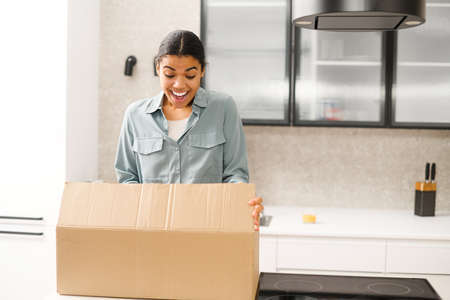 Multiracial woman unpacking parcel cardboard box with online order. Satisfied biracial young woman...