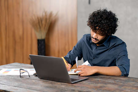 Online training. Young guy student with curly hair studying at home while sitting in the modern room...