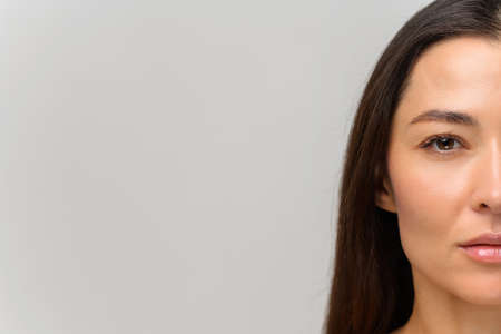 Cropped portrait of attractive asian woman with naked shoulders looking at the camera. Half face of serious beautiful female with smooth face skin and natural make-up, straight healthy hair isolatedの写真素材