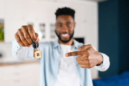 Relocation concept. Headshot of excited male moving in new home or apartment. Cheerful multiracial man homeowner looking at camera and points finger at the keys with keychain in his handの写真素材