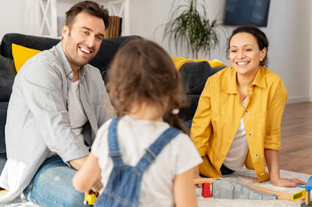 Love and care concept. Two parents looking at the little toddler daughter playing on the floor sitting back to camera, happy mother and father spending time together with kidの写真素材