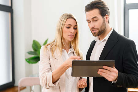 Waist up portrait view of the modern woman and man in formal wear using digital tablet at the office. Portrait of female and male office employees using online technology for doing businessの写真素材