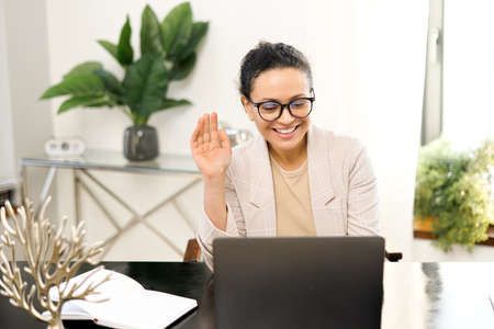 Video meeting concept. Cheerful middle-aged woman holding video call on the laptop at office, waving...