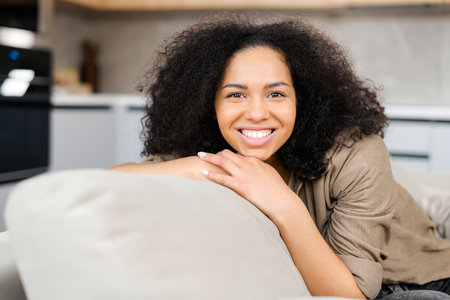 Portrait of charming multiracial woman with brunette hair. Smiling female sitting on the couch and...