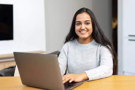 Beautiful and clever young middle eastern girl wearing casual clothes is using a laptop in cozy...