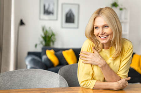 Close-up portrait on blonde-haired woman in home interior. Charming mature caucasian lady looking...