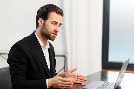 Side view of caucasian office employee talking via video connection while sitting at the desk. A guy...
