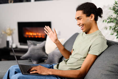Video communication, zoom. Side view of the multiracial young guy uses a laptop for a video call at...