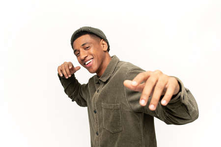 Excited positive hispanic man in stylish clothes dancing, raising hands up and having fun, good mood. Indoor studio shot isolated on white backgroundの写真素材