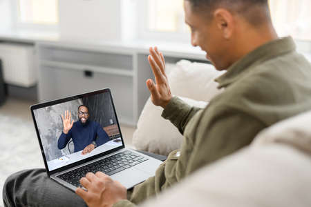 Hello. Side view of the smiling and cheerful young man using laptop for video call at the...