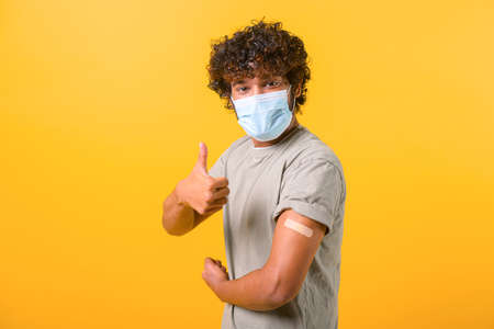 Curly Indian guy in medical mask got an injection and has patch on his forearm, vaccinated man...