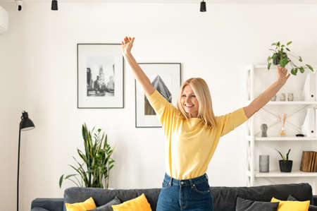 Charming elegant mature middle-aged businesswoman smiling, sitting in the modern house, wearing yellow sweater. Happy people conceptの写真素材