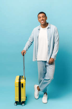 Full length photo of smiling young African-American guy in casual denim wear standing with yellow...