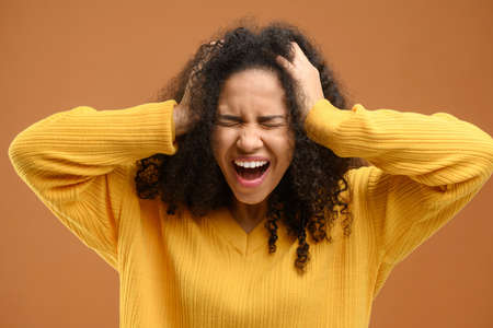 Multiracial beautiful curly hair woman over brown background celebrating mad and crazy for success...