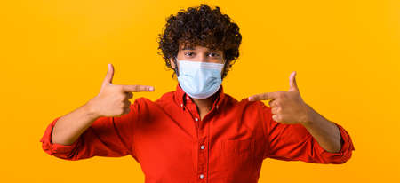 Protect yourself during pandemic. Indian young man points fingers on medical mask on his face....