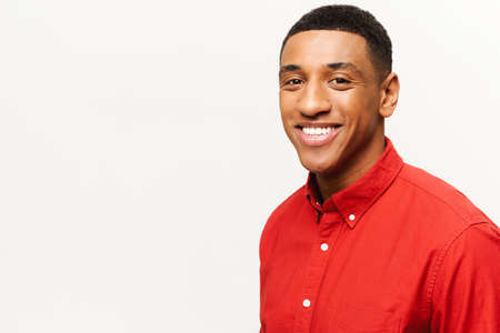 Headshot of friendly optimistic African-American guy in red shirt isolated on white. Smiling kind...