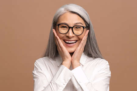 Portrait of excited overjoyed business woman with grey hair standing with raised arms and shouting...