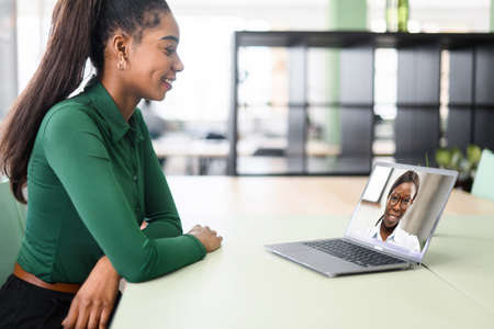 Two female coworkers talking through video call. Business women using app on laptop for video chat,...