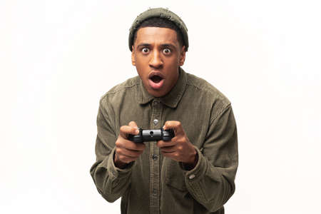 Excited young multiracial man playing video games and looking at camera with surprised face, holding...