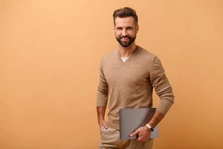Working with joy. Smiling cheerful business man wearing pullover sweater, standing with laptop, pc...