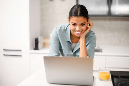 Smiling and concentrated businesswoman in casual wear is looking at the laptop screen, solving tasks, freelance woman working remotely from homeの写真素材