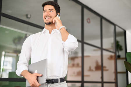 Ambitious handsome hispanic male entrepreneur, start-up owner in white shirt standing with laptop in...
