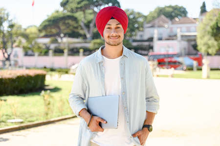 Working with joy. Smiling cheerful Indian freelancer man wearing traditional headwrap turban...