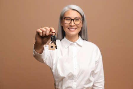 Senior happy woman hold keys of apartments and rejoicing isolated on beige background. People lifestyle conceptの写真素材