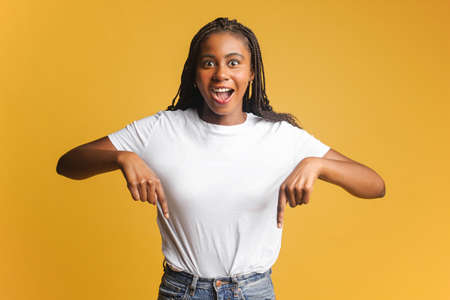 Excited positive woman pointing fingers down showing space for your advertisement, looking at camera...