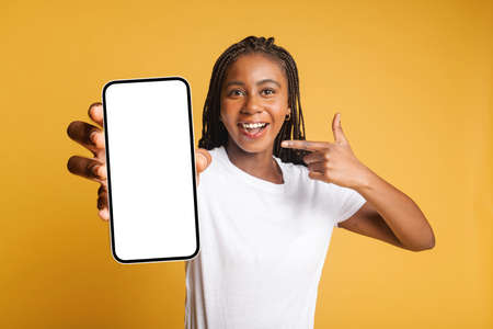 Surprised with ability of new app on the smartphone young attractive woman points finger on it, a female holds a phone, got an unexpected message or notification, looks at the camera amazed, isolatedの写真素材