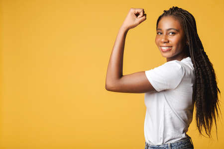Female power. Young african-american woman showing bicep and looking at the camera isolated on...