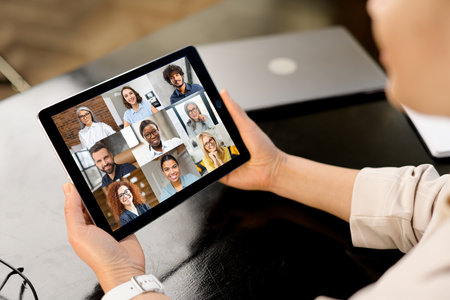 Woman participates in video conference with multiracial team, virtual meeting on the digital tablet, e-learning. Female employee talking online with group of diverse colleagues or work teamの写真素材