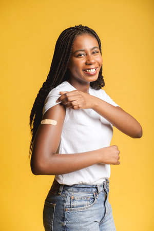 Happy young african-american woman demonstrating medical patch aid on the forearm standing isolated on yellow, got a vaccination, recommending keep self in safety from viral diseaseの写真素材