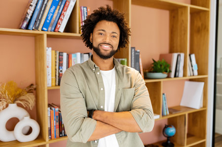 Cheerful African-American modern businessman, happy guy with curly hairstyle stands in contemporary...