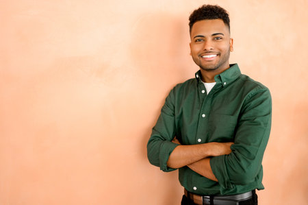 Successful confident young indian male entrepreneur or businesswoman in casual clothes standing with arms folded over orange background, looking at the camera with attractive smileの写真素材