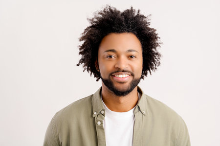 Portrait of happy satisfied handsome young man in casual wear standing and looking at camera with toothy smile. Indoor studio shot on white backgroundの写真素材