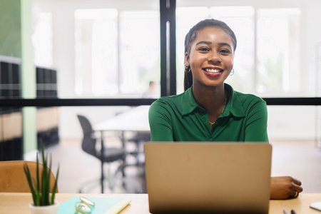 Portrait of concentrated african-american female employee using laptop computer, smiling black businesswoman responds emails, freelancer woman working on the distance sitting in coworking spaceの写真素材