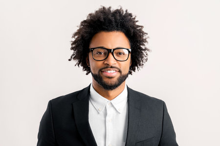 Close-up portrait of middle-aged curly african-american businessman in formal office suit and elegant eyeglasses looking at camera smiling isolated on white, profile photo of manager or male employeeの写真素材