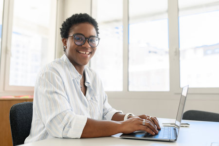 Side view at stylish african american business woman with short haircut in casual outfit sitting in...