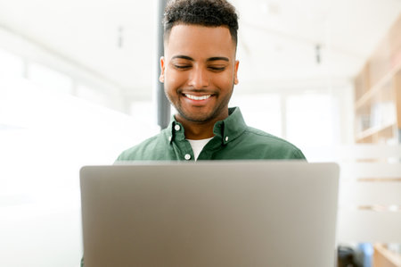 Friendly and cheerful young indian businessman using laptop for office work, male employee checks...