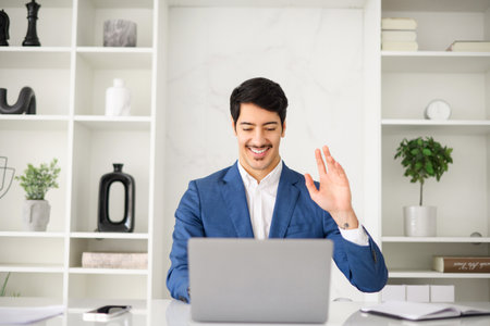A charismatic Hispanic businessman makes a welcoming gesture during a video call, exemplifying the...