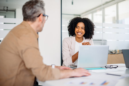 A joyful female professional with curly hair shares a warm smile while engaging in a productive...