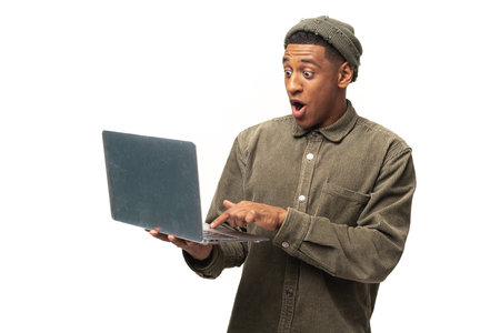 Portrait of shocked surprised man holding laptop and looking at the display with big astonished...