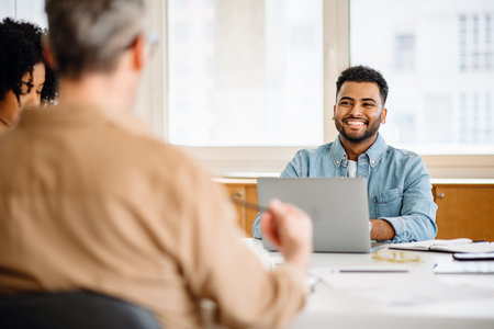 A young Latin man in casual wear, with a beaming smile participates in a meeting, his attentiveness and joy reflecting the positive dynamics of a diverse and modern office team.の写真素材