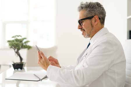 With a gentle smile, the doctor interacts with a smartphone during a consultation, highlighting the ease with which experienced professionals adapt to and utilize new healthcare technologies.の写真素材