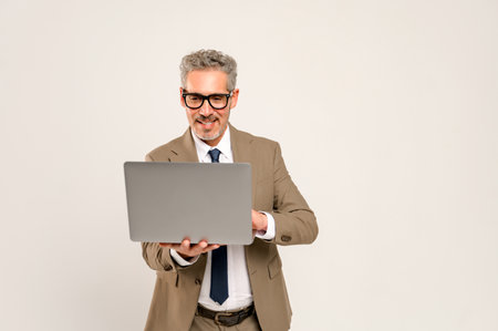 A charismatic grey-haired businessman looking at a laptop screen. This image captures the essence of modern business presentations or online communication, perfect for concepts related to technologyの写真素材